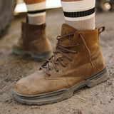 Person wearing 5.11 Tactical Rambler 6-inch Boots in Dark Coyote with striped crew socks, standing on a dirt track beside a muddy off-road vehicle tyre